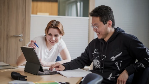 Zwei Personen sitzen an einem Tisch und schauen zusammen auf ein Tablet.