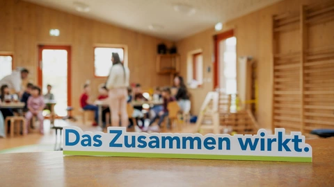 Schriftzug „Das Zusammen wirkt.“ im Vordergrund, im Hintergrund Kinder und Erwachsene in einer CJD-Einrichtung, Gemeinschaft und Teilhabe.