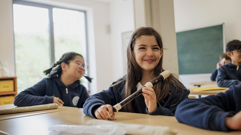 Ein Mädchen lächelt im Klassenzimmer mit Blockflöte – musikalische Bildung im CJD. Jetzt kreative Angebote entdecken!