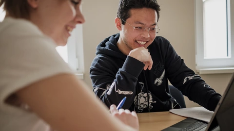 Zwei fröhliche, junge Menschen schauen auf einen Laptop
