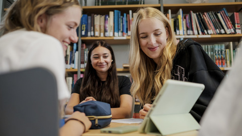 Drei Schülerinnen schauen gemeinsam in ein Tablet und lachen