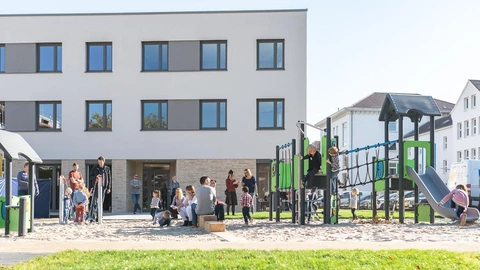 Ein sehr moderner Spielplatz auf dem viele Kinder mit ihren Familien spielen.