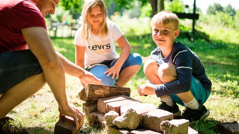 Zwei Kinder und ein Erwachsener knien neben einem kleinen Steinhaufen.