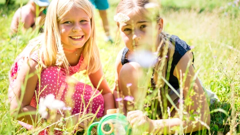 Zwei Kinder knien mit einer Becherlupe auf der Wiese