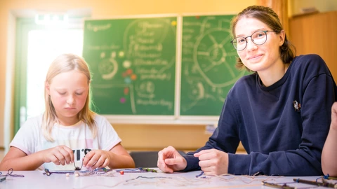 Ein Kind und eine junge Frau sitzen am Tisch. Vor ihnen liegen Bastelmaterialien.