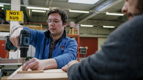 Zwei Männer arbeiten zusammen in einer Werkstatt und benutzen einen Akkuschrauber.