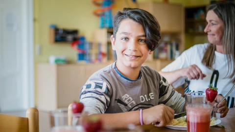 Ein Junge sitzt am Essenstisch neben einer Pädagogin.