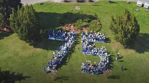 Aus der Luftperspektive ist eine große Menschenmenge vor einem historischen Gebäude zu sehen, die die Zahl „75“ formt. Viele Teilnehmende tragen bunte Luftballons in Blau, Grün und Gelb, wodurch die Jubiläumszahl eindrucksvoll hervorgehoben wird. Die Aktion auf der Rasenfläche markiert das 75-jährige Bestehen des CJD und symbolisiert Gemeinschaft, Zusammenhalt und Feierlichkeit.