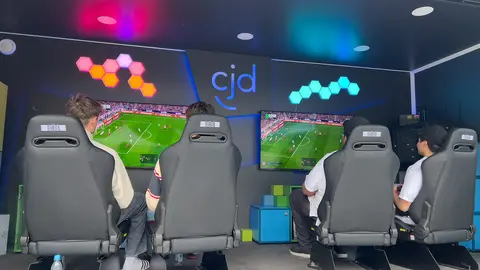 Einblick in den Game4All-Anhänger. 4 Personen sitzen auf 4 Gaming-Stühlen. Auf 2 Monitoren ist ein FIFA-Spiel zu sehen.