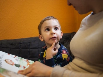Neugieriger Junge liest mit einer Erzieherin aus einem Buch