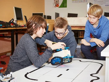 Drei Jugendliche basteln gemeinsam an einem Roboter