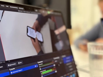Auf einem Notebook-Bildschirm ist zu sehen, wie eine Person ein Smartphone bedient