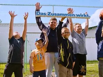 Mehrere Kinder und ein Erzieher des CJD jubeln und halten ein Schild mit dem CJD-Motto Das Zusammen wirkt