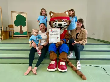 Maskottchen Muskelkater mit zwei Frauen und drei Kindern bei der Zertifikatsübergabe