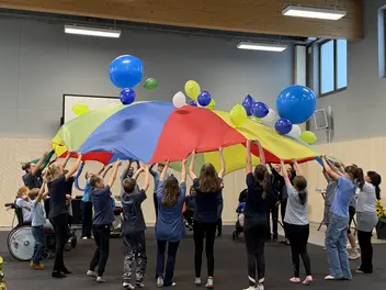 Schüler und Pädagogen werfen mit einem großen, bunten Schwungtuch Luftballons nach oben.