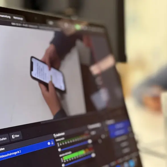 Auf einem Notebook-Bildschirm ist zu sehen, wie eine Person ein Smartphone bedient