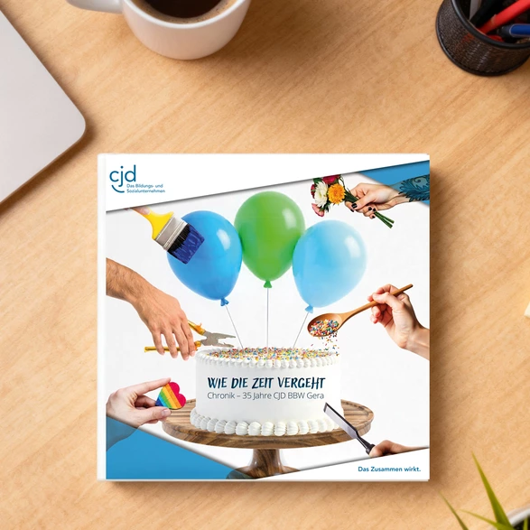Auf einem Schreibtisch liegt eine Broschüre mit dem Titel "Wie die Zeit vergeht / Chronik – 35 Jahre CJD BBW Gera".