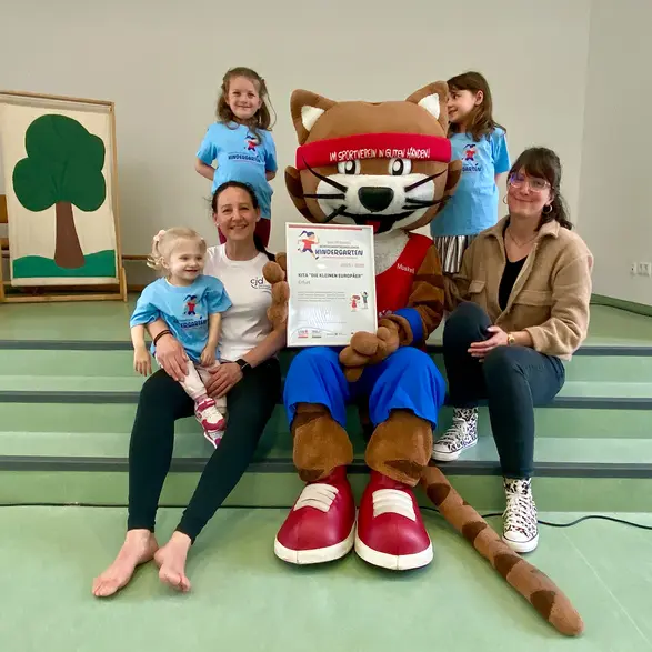 Maskottchen Muskelkater mit zwei Frauen und drei Kindern bei der Zertifikatsübergabe