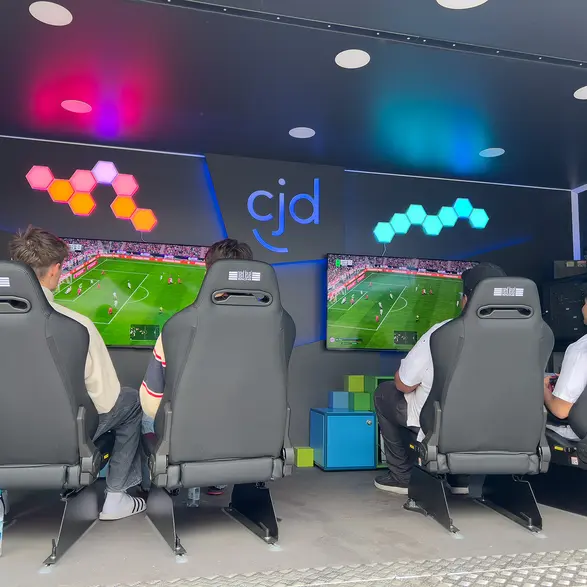 Einblick in den Game4All-Anhänger. 4 Personen sitzen auf 4 Gaming-Stühlen. Auf zwei Monitoren ist ein FIFA-Spiel zu sehen.