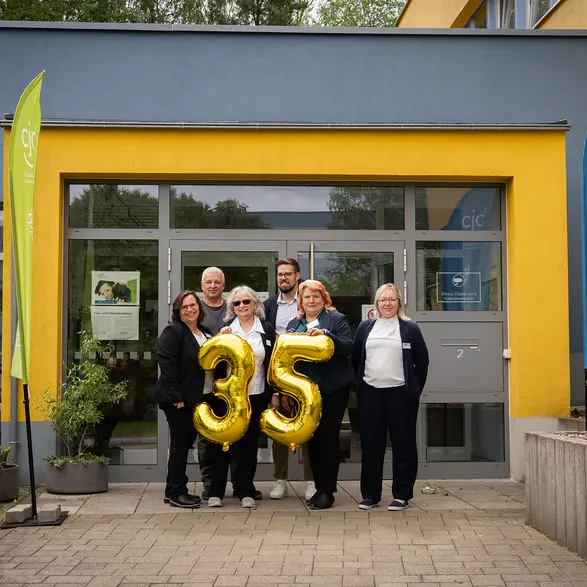 Sechs Personen stehen vor dem Eingang des CJD in Ilmenau. Sie halten große, goldene Folienballons 35.