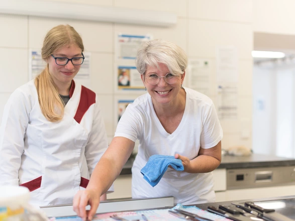 Eine CJD Ausbilderin im Bereich Hauswirtschaft zeigt einer jungen Auszubildenden, wie man Besteck poliert.