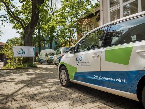 CJD-Fahrzeug mit Logo und Slogan „Das Zusammen wirkt.“ vor einer Einrichtung, Mobilität und Teilhabe im CJD.