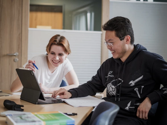 Eine junge Frau und ein junger Mann sitzen gemeinsam an einem Tisch und lernen an einem Tablet und mit Büchern und Notizheften. Spenden stärken die Bildung von jungen Menschen in unseren Einrichtungen.
