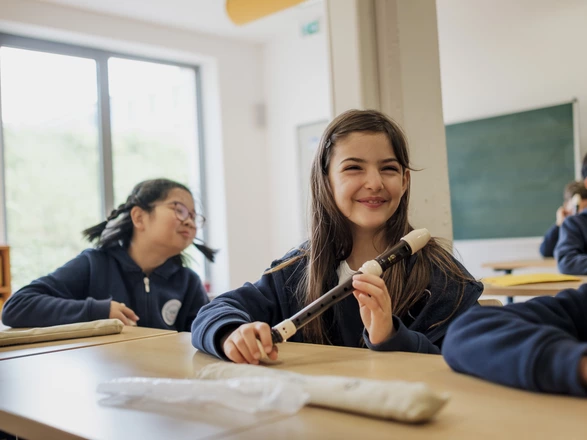 Bild aus dem Musikunterricht in der Schule, eine Schülerin lacht in die Kamera, während sie eine Flöte hält