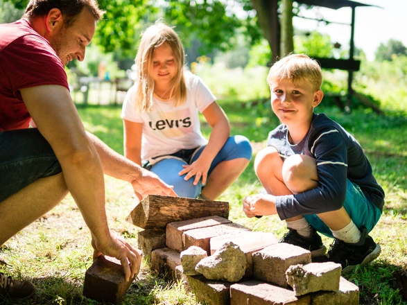 Zwei Kinder und ein Erwachsener knien neben einem kleinen Steinhaufen.