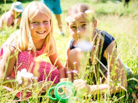 Zwei Kinder knien mit einer Becherlupe auf der Wiese