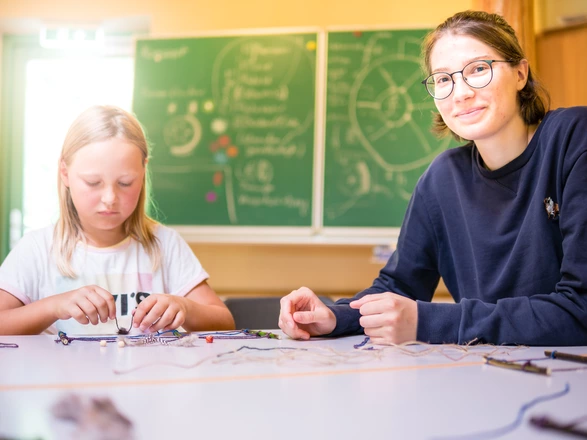 Ein Kind und eine junge Frau sitzen am Tisch. Vor ihnen liegen Bastelmaterialien.