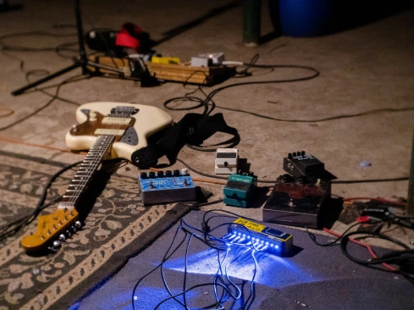 Auf einem Teppich liegen eine E-Gitarre sowie mehrere Effektgeräte, die über Kabel miteinander verbunden sind. Die Szene vermittelt den Eindruck einer Probe oder eines Auftritts, bei dem ein Geburtstagslied vorbereitet oder gespielt wird. Die lose angeordneten Instrumente und Kabel unterstreichen die kreative, spontane Atmosphäre einer musikalischen Darbietung im Rahmen des 75-jährigen CJD-Jubiläums.