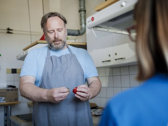 Ein CJD Werkstattpädagoge zeigt einer jungen Frau Lebensmittel in einer Großküche.