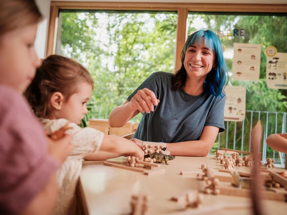 Eine CJD Erzieherin spielt mit zwei Mädchen ein Holz-Bausteine-Spiel in einer CJD Kita.