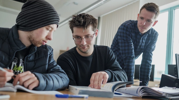 Zwei junge Männer lernen gemeinsam und werden dabei von einem Lehrer unterstützt. Spenden stärken Bildung und individuelle Förderung von jungen Menschen im CJD.