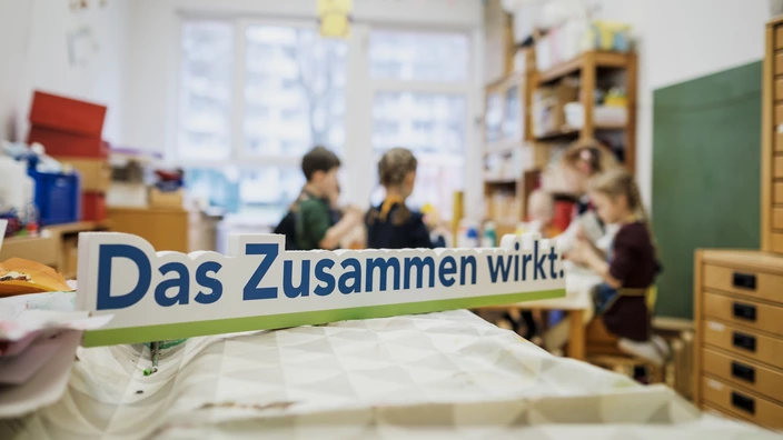 Schriftzug „Das Zusammen wirkt.“ im Vordergrund, unscharfe Kinder im Hintergrund, Gemeinschaft beim CJD.