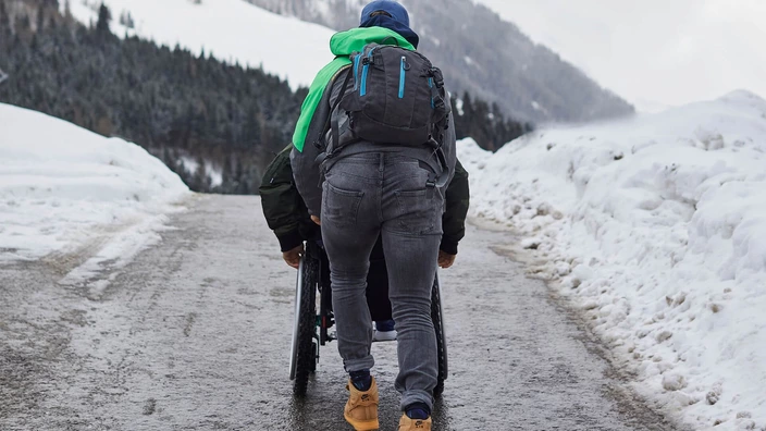 Junger Mann schiebt im Winter einen Rollstuhlfahrer die Straße hinauf