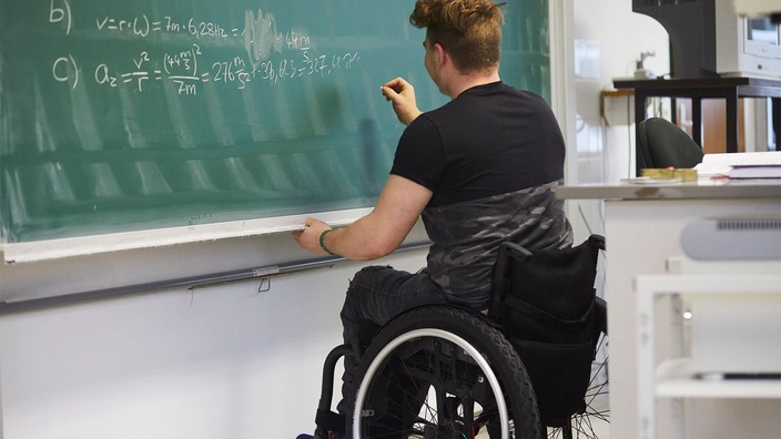 Nikolai Sommer sitzt in einem Rollstuhl und schreibt mit dem Rücken zur Klasse etwas an die Tafel