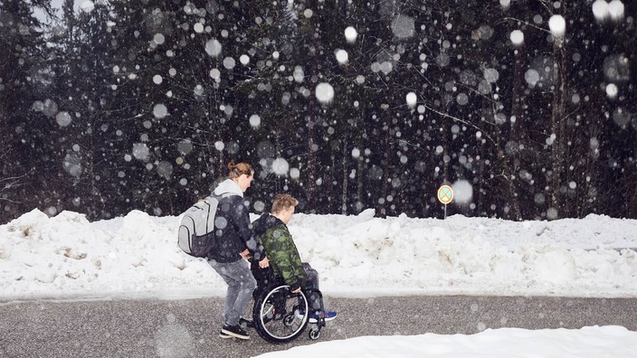 Nikolai Sommer wird in winterlicher Landschaft von einem Mitschüler im Rollstuhl geschoben