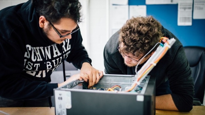 Zwei Auszubildende betrachten einen aufgeschraubten Computer