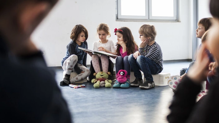 Kinder sitzen gemeinsam in einem Raum und betrachten ein Bilderbuch
