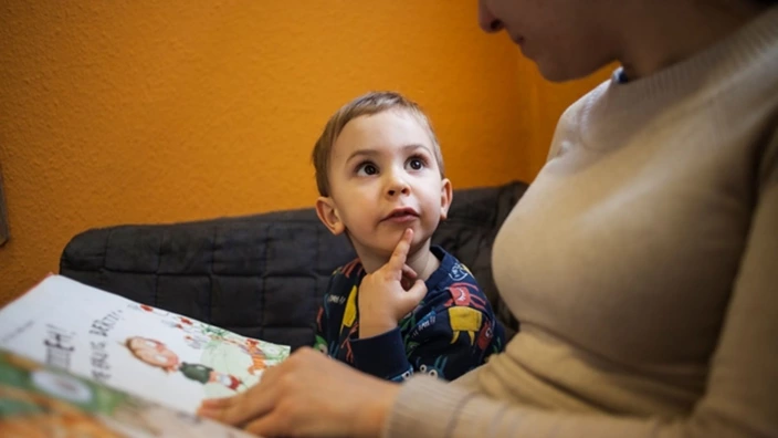 Neugieriger Junge liest mit einer Erzieherin aus einem Buch