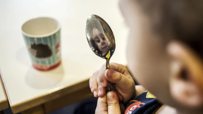 Kleiner Junge betrachtet sein Spiegelbild in einem Löffel