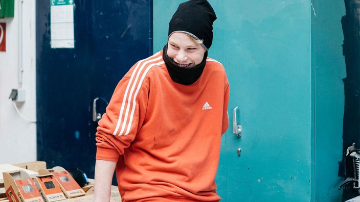 Lachender junger Mann im orangenen Pullover in der Werkstatt