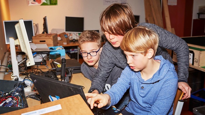 Drei Jugendliche schauen gebannt in einen Laptop