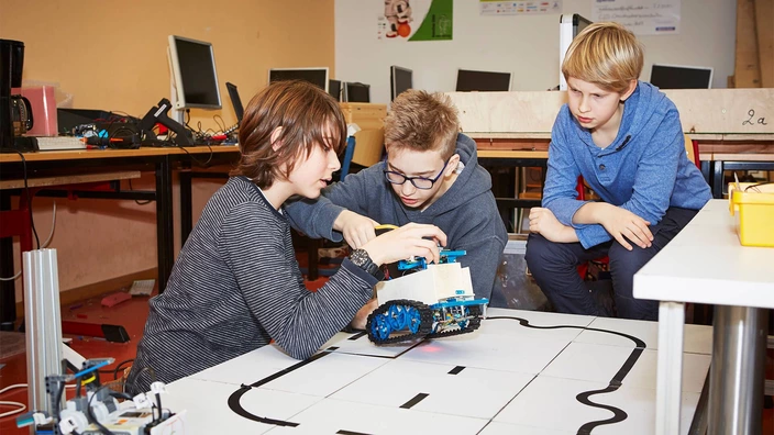 Drei Jugendliche basteln gemeinsam an einem Roboter