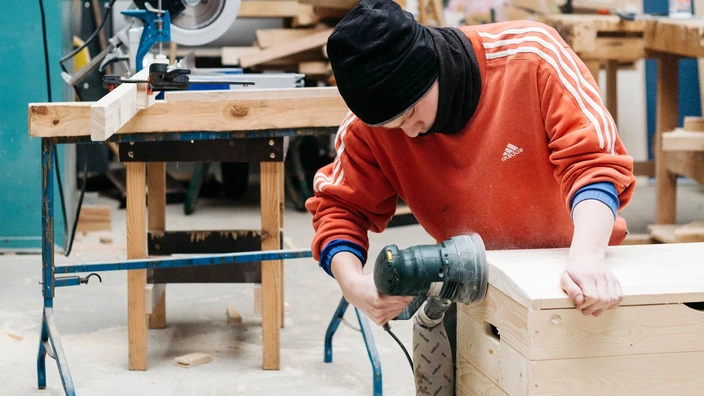 Junger Mann schleift eine Holzkiste ab