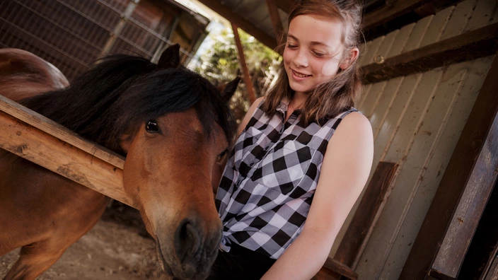 Eine Jugendliche streichelt ein braunes Pferd in einem Stall. Spenden helfen Orte der Geborgenheit für junge Menschen zu schaffen.
