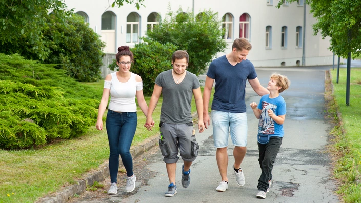 Vier Personen laufen nebeneinander einen Weg entlang. 