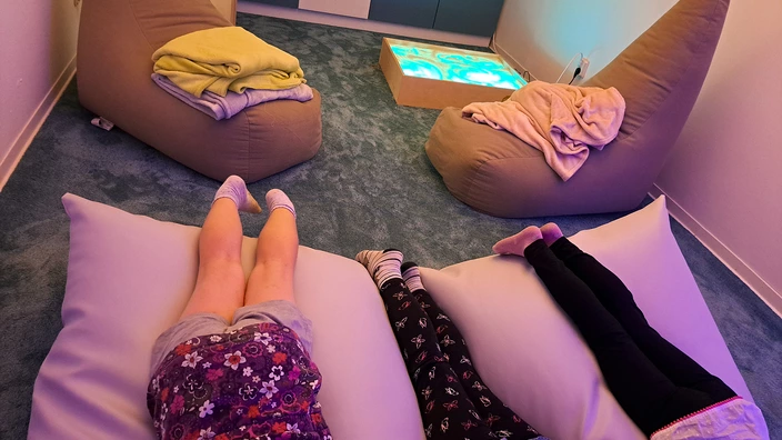 In einem gemütlich eingerichteten Raum zum Snoezelen liegen 3 Kinder auf einem Sitzsack. Zu sehen sind nur die Beine der Kinder.
